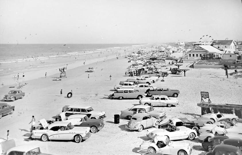 beach with many 1950's style cars and a Ferris wheel in the distance