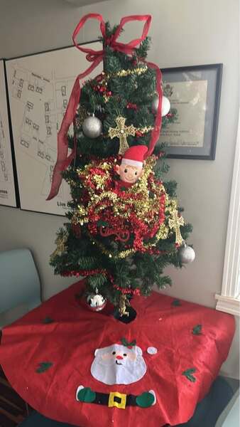 A small Christmas tree sits on a table with an elf toy tangled in the red and gold garland