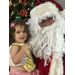 A little girl with brown curly hair sits on Santa's lap